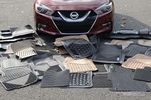 Lots of scattered car floor mats on the ground in front of a fed sedan.