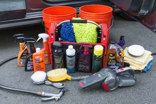 assortment of products brushes and buckets on the ground in front of a car